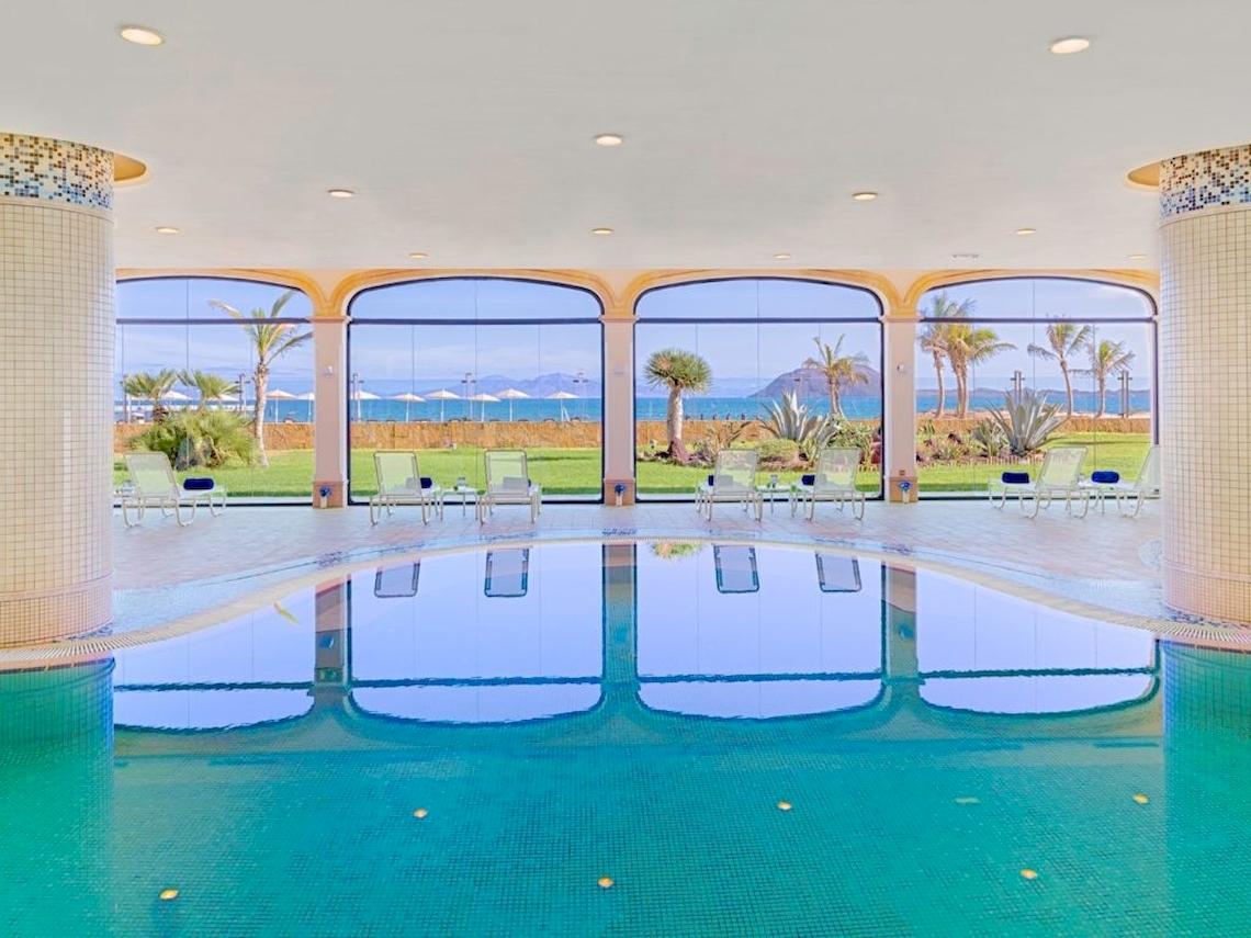 Poolbereich im Secrets Bahia Real Resort & Spa mit Blick auf das Meer und Palmen