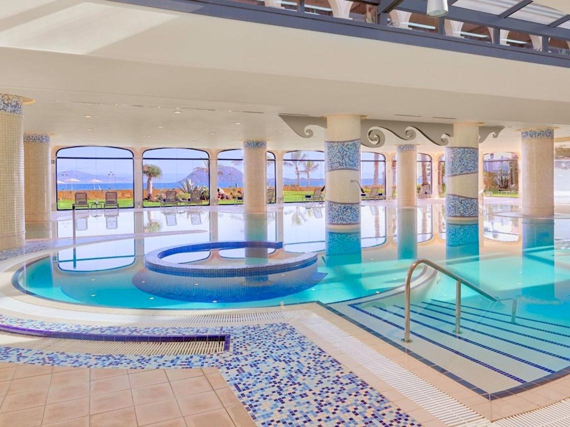 Ein großer Swimmingpool im Secrets Bahia Real Resort & Spa mit blauen Fliesen und Blick auf das Meer.