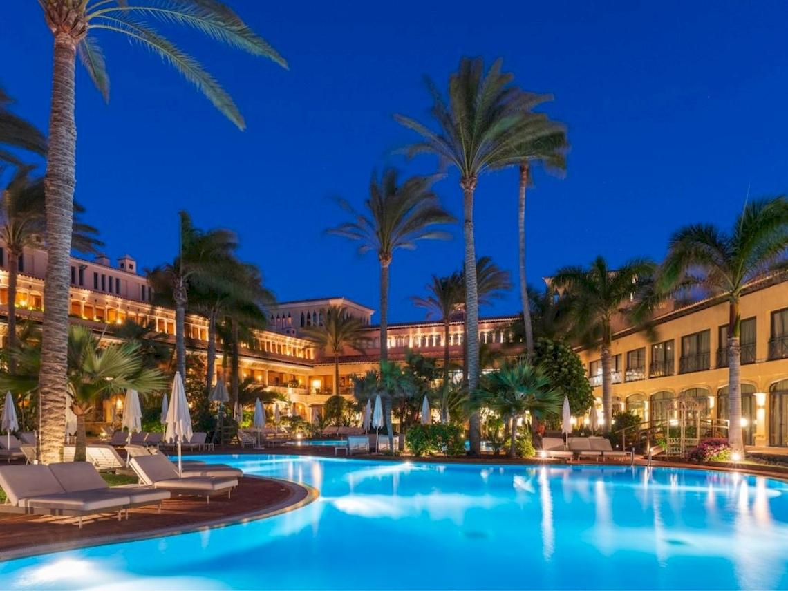 Nachtansicht des Swimmingpools des Secrets Bahia Real Resort & Spa mit Loungeliegen und Palmen