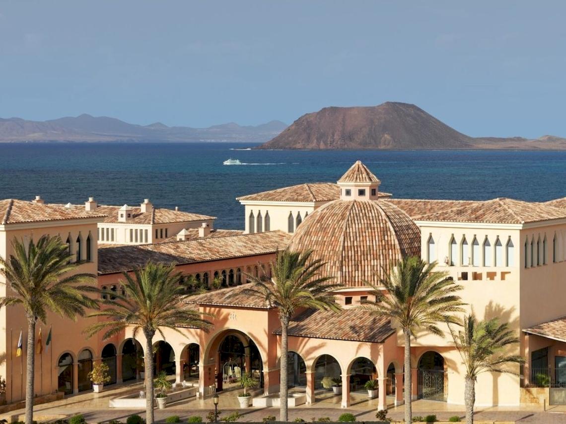 Außenansicht des Secrets Bahia Real Resort & Spa mit Blick auf das Meer und die Berge
