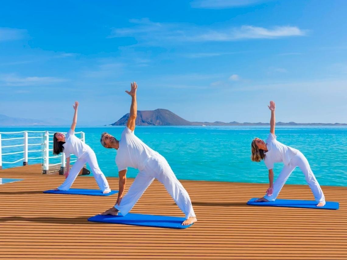 Drei Personen machen Yoga auf einer Plattform am Pool im Gewässer