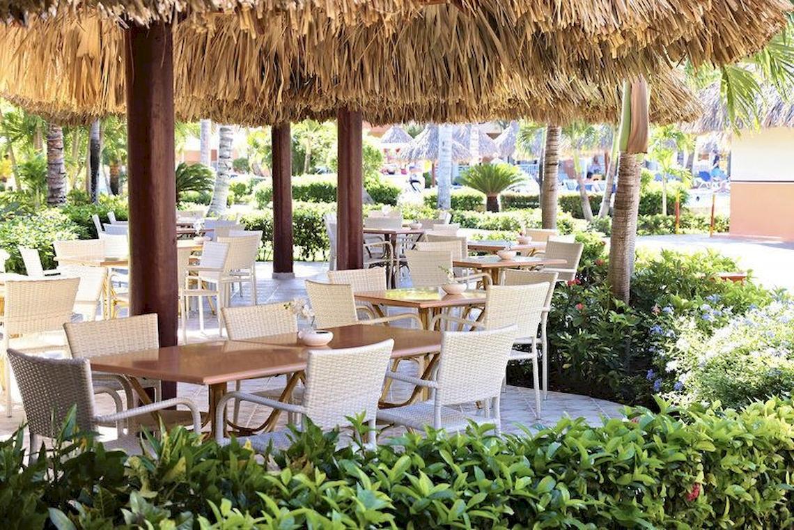 Außenbereich des Bahia Principe Grand Turquesa Hotels mit Tisch und Stühlen unter Strohdächern.