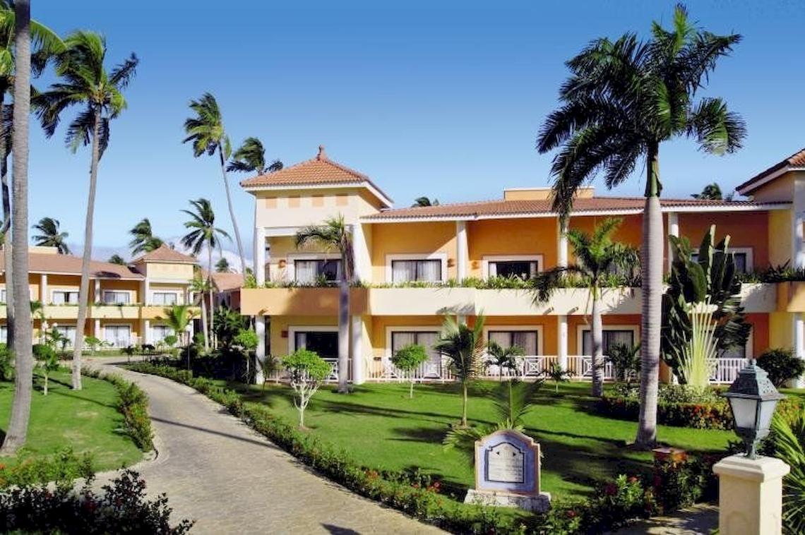 Außenansicht des Bahia Principe Grand Turquesa Hotels mit mehreren Stockwerken, gelben Wänden und Palmen im Vordergrund.