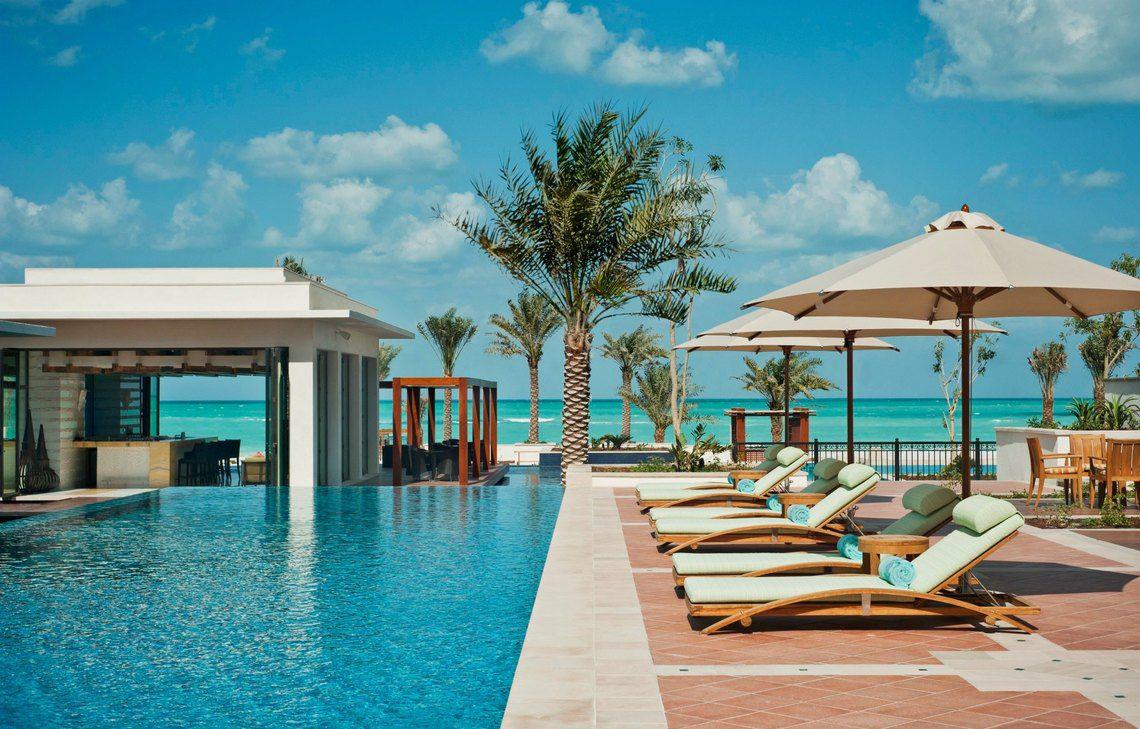 Poolbereich im St. Regis Saadiyat Island Resort mit Loungeliegen und Palmen