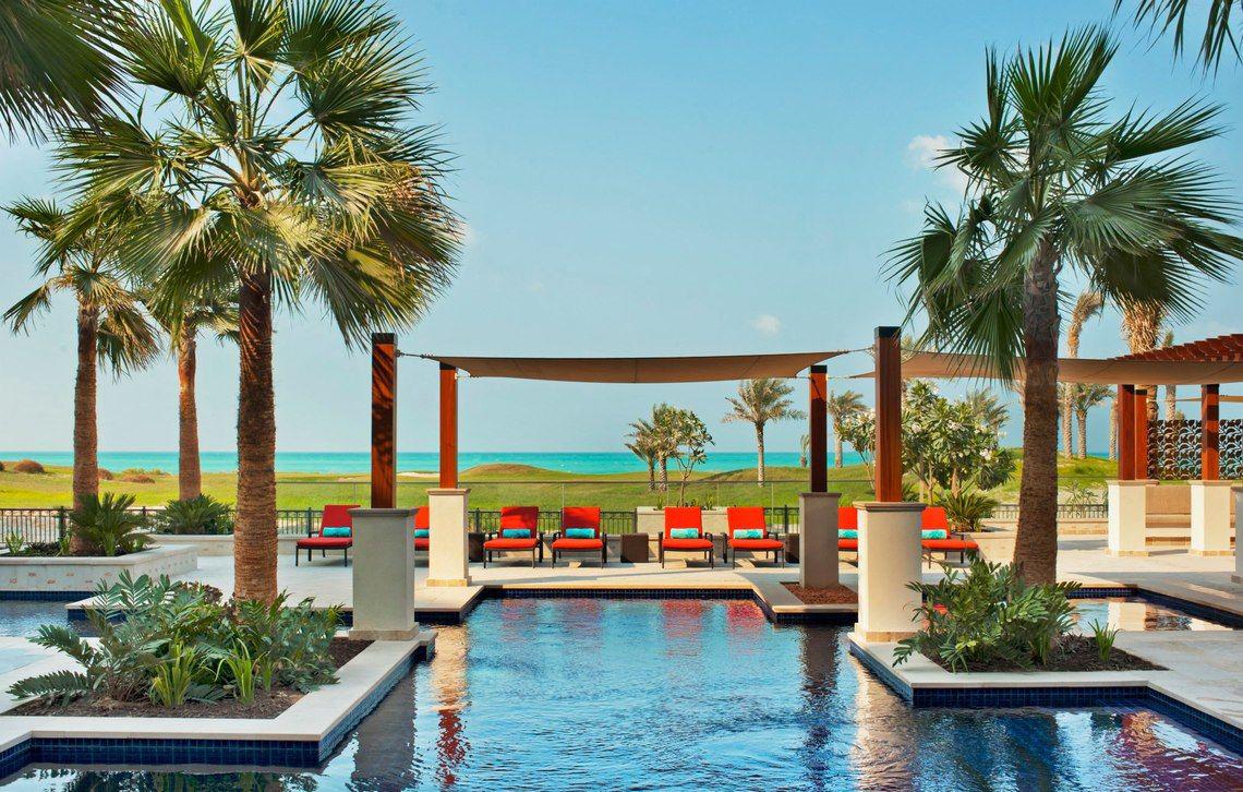 Pool-Lounge-Bereich im St. Regis Saadiyat Island Resort mit roten Sesseln und Palmen.