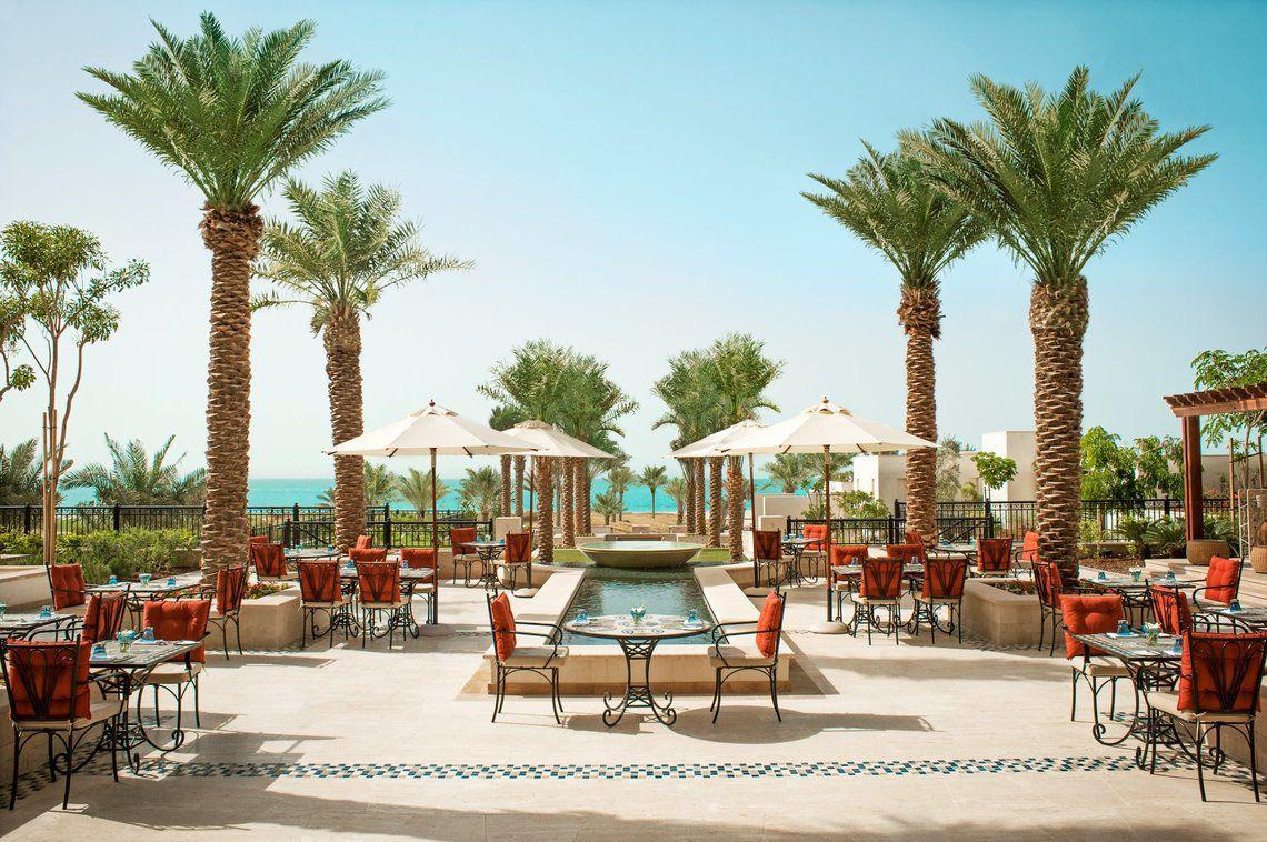 Außenbereich des St. Regis Saadiyat Island Resorts mit Tischen, Stühlen und Palmen