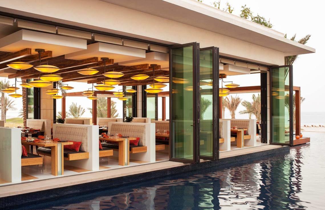 Poolside-Restaurant im St. Regis Saadiyat Island Resort mit offenen Glastüren und Tischen.