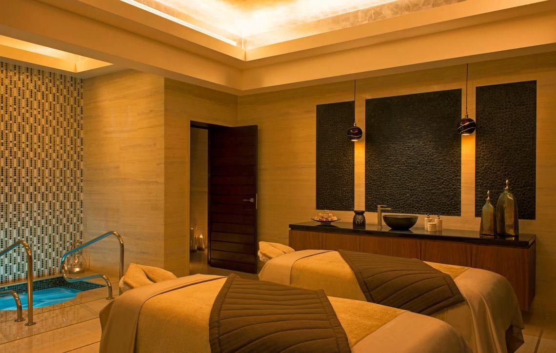 Behandlungsraum im Spa des St. Regis Saadiyat Island Resort mit zwei Massageliegen, einem kleinen Pool und einem Eingang.