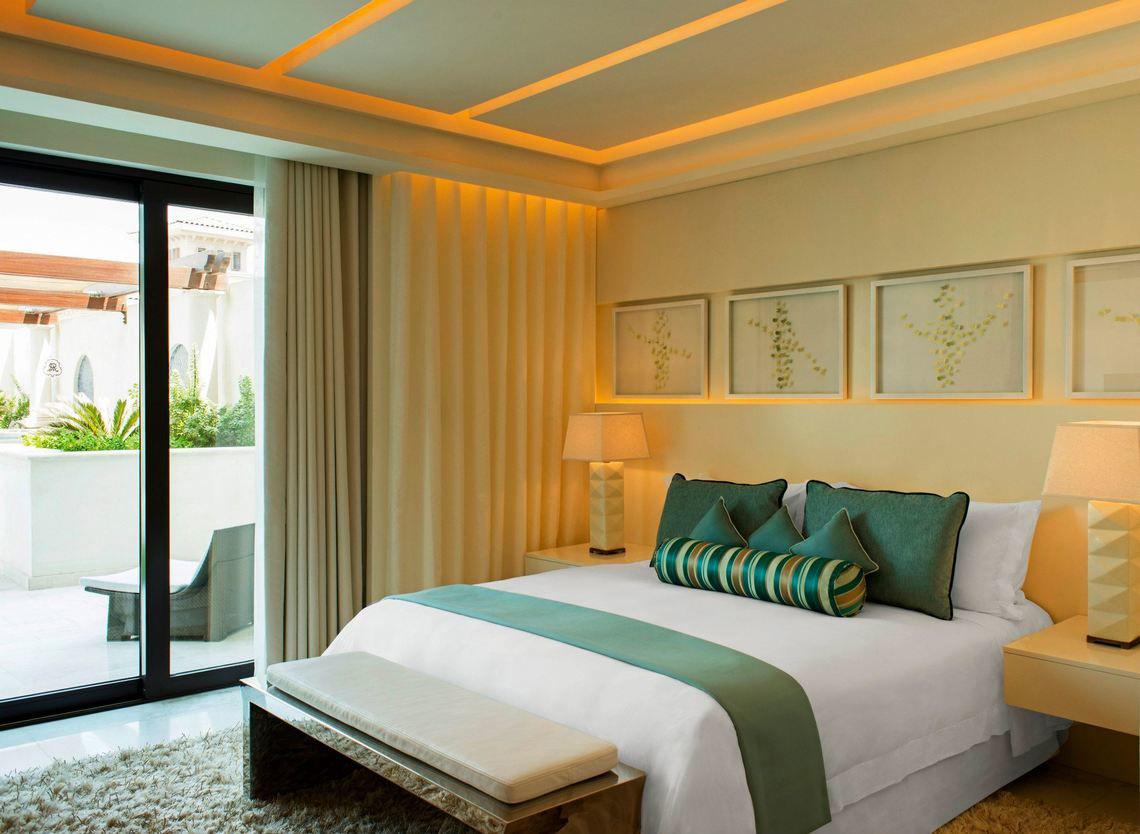 Schlafzimmer im St. Regis Saadiyat Island Resort mit einem großen Bett, grünen Kissen und einem offenen Balkon.