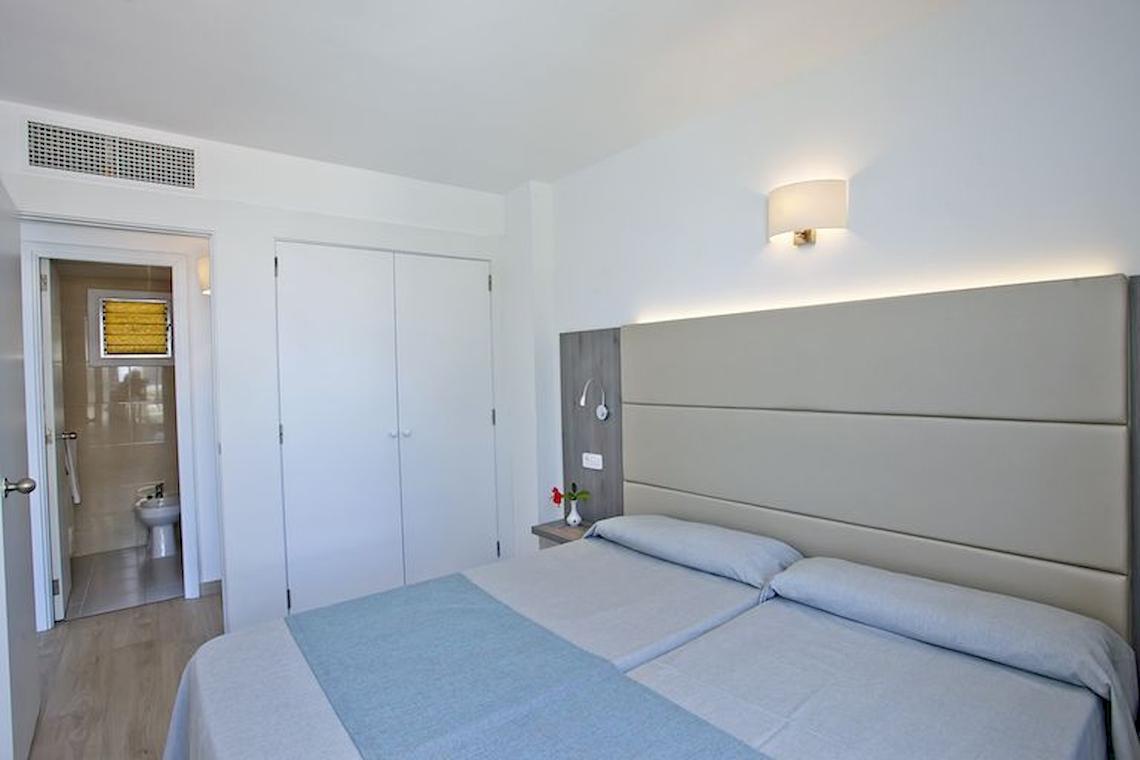 Schlafzimmer im Playa Dorada Aparthotel mit zwei Betten, weißen Wänden und einem Badezimmer.