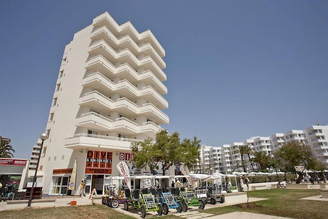 Außenansicht des Playa Dorada Aparthotels mit mehreren bunten Golfcarts vor dem Gebäude.