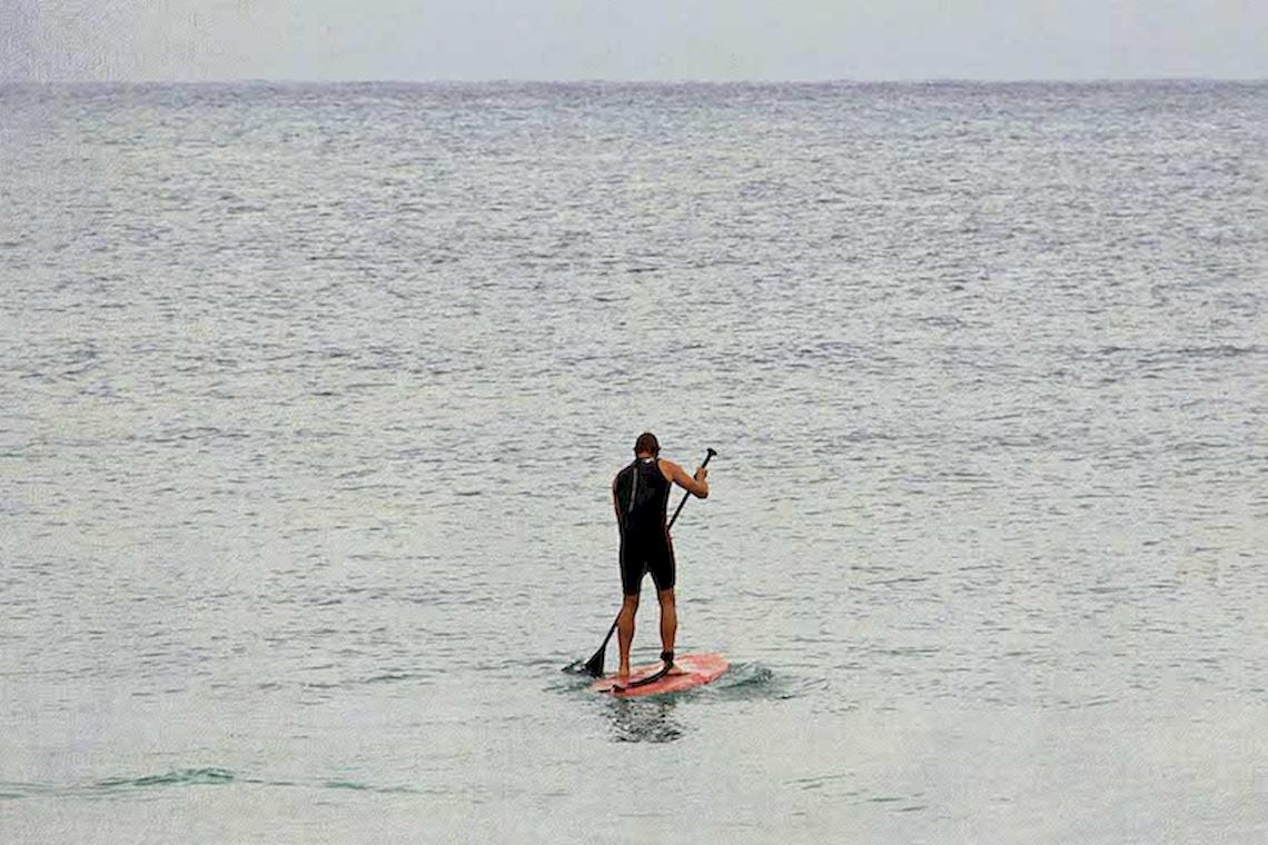Ein Mann steht auf einem roten Surfbrett und paddelt auf dem offenen Meer.