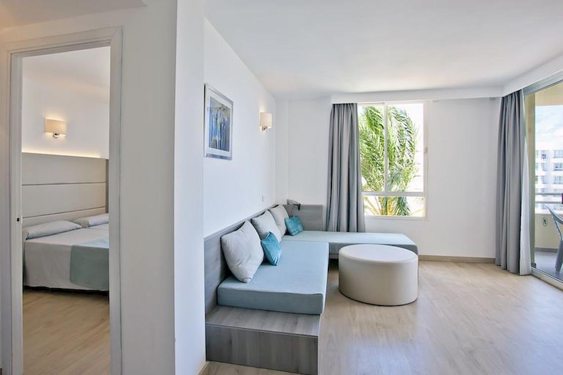 Innenansicht eines Zimmers im Playa Dorada Aparthotel mit Doppelbett, Sofa und Fenstern.