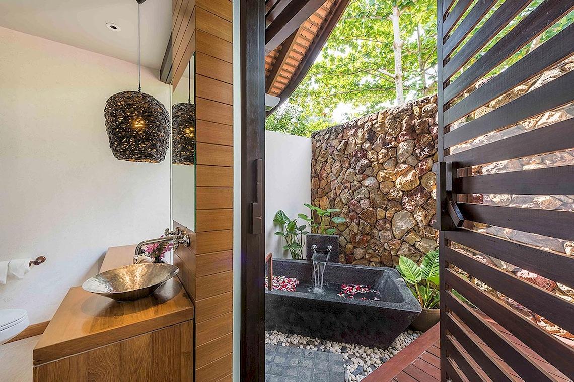 Ein Badezimmer im Tubkaak Krabi Boutique Resort mit einer freien Badewanne, einer Steinmauer und einer Holzdecke.