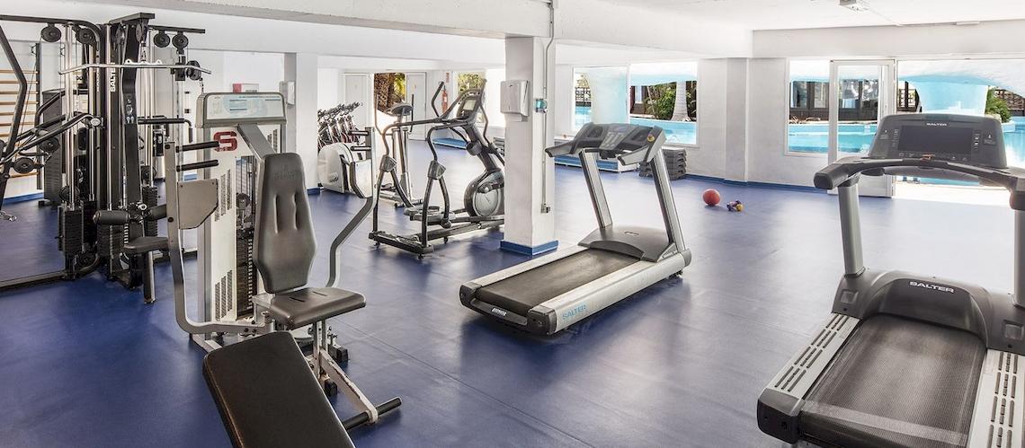 Fitnessstudio im Fuerteventura Princess Hotel mit verschiedenen Geräten und Blick auf den Pool.