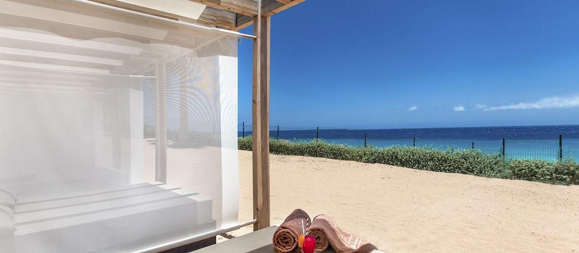 Außenbereich des Fuerteventura Princess Hotels mit einem Strandbett, Strandtüchern und einem kühlen Getränk.