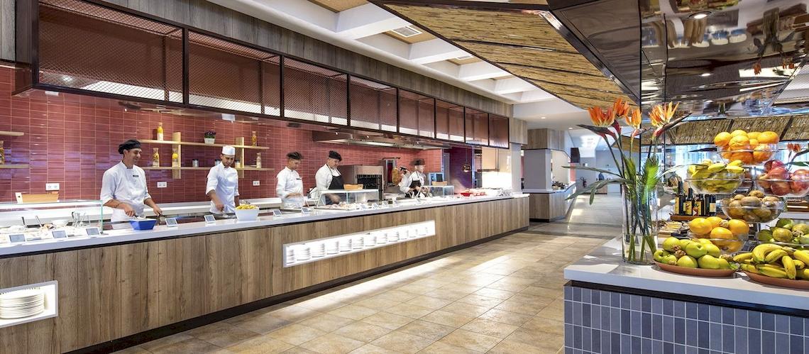 Innenansicht des Restaurants im Fuerteventura Princess Hotel mit Köchen, die an einer langen Theke arbeiten und verschiedene Früchte auf dem Tisch sind.