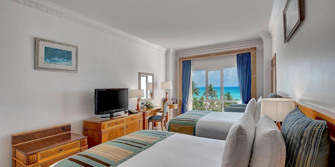 Doppelzimmer im Crowne Plaza Resort Salalah mit Meerblick, zwei Betten, Fernseher, Schreibtisch und Ausblick auf das Meer.