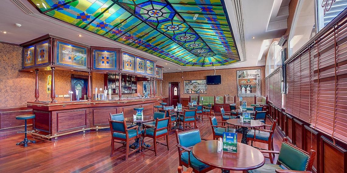 Innenansicht des Crowne Plaza Resort Salalah Bar mit Holzboden, bunten Stühlen und Tischen.