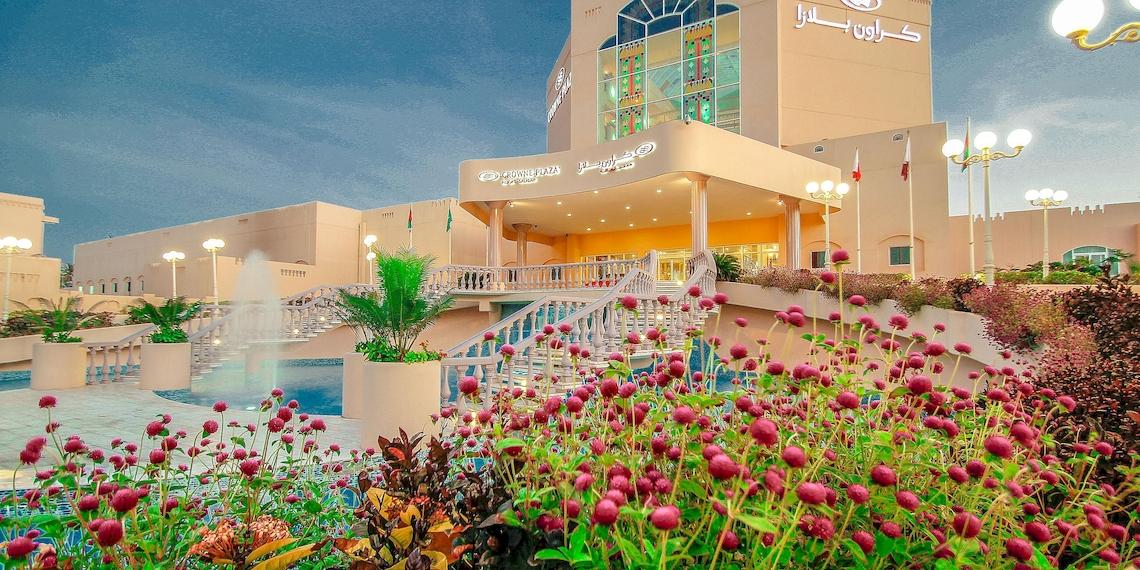 Außenansicht des Crowne Plaza Resort Salalah mit Swimmingpool und Blumenbeet.