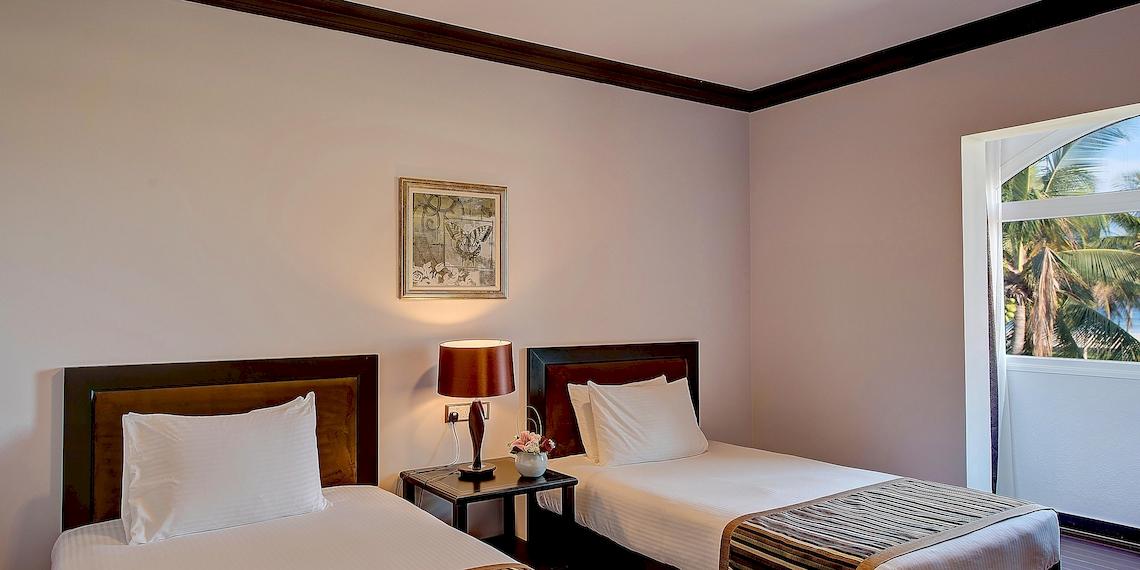 Zwei Betten in einem Zimmer im Crowne Plaza Resort Salalah mit Aussicht auf Palmen und Meer.