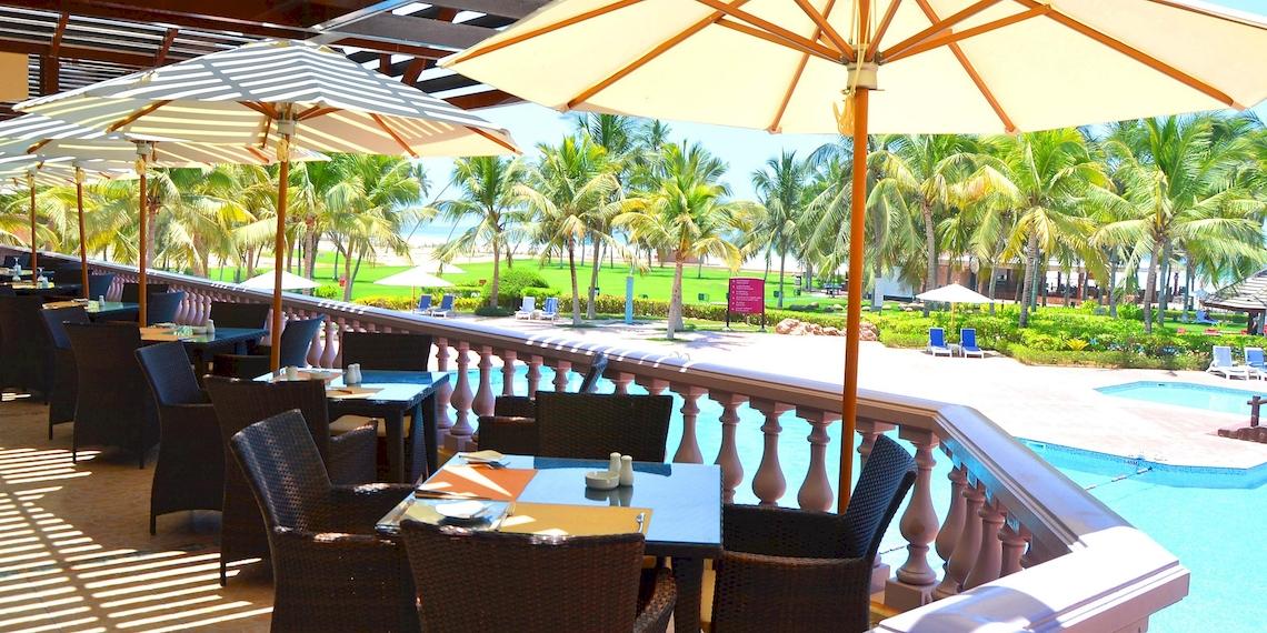 Poolterrasse des Crowne Plaza Resort Salalah mit Tischen, Stühlen und Sonnenschirmen