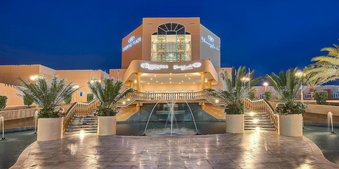 Außenansicht des Crowne Plaza Resort Salalah mit Brunnen, Pflanzen und beleuchteter Fassade bei Nacht