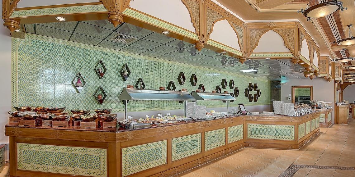 Innenbereich des Restaurants im Crowne Plaza Resort Salalah mit grünen Fliesen und Holzdekoration.