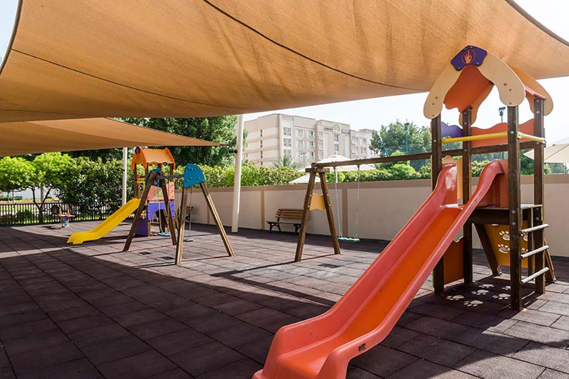 Kinderspielplatz unter einem Sonnensegel mit Rutschen und Schaukeln im Freien.