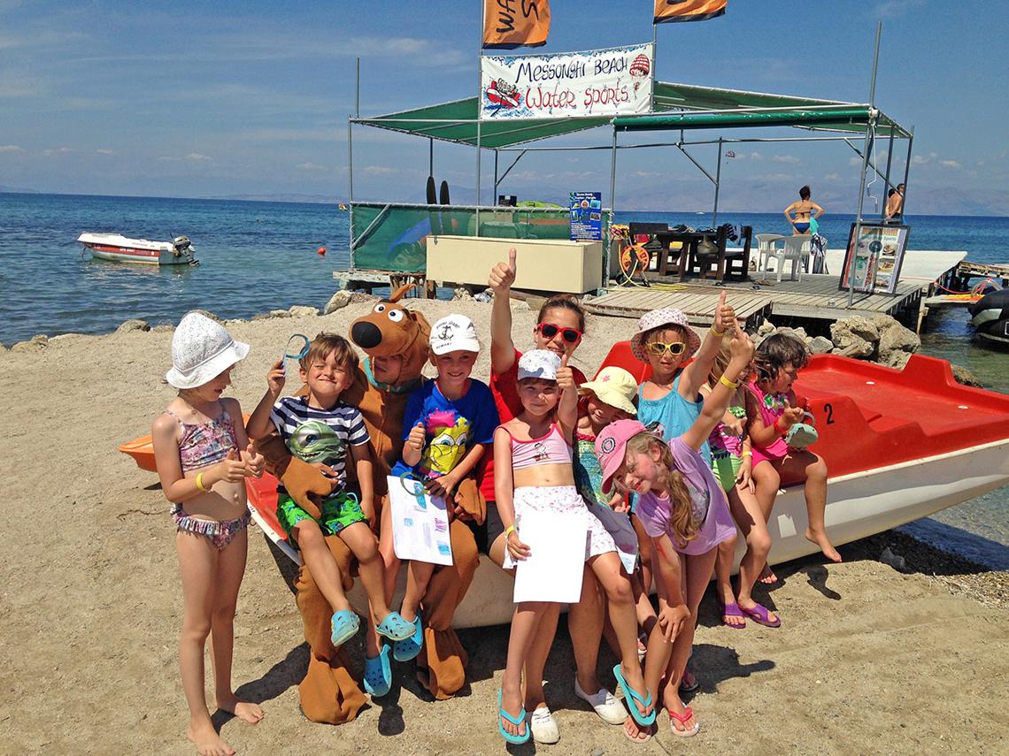 Kinder mit Maskottchen auf dem Strand neben einem Wassersport-Boot
