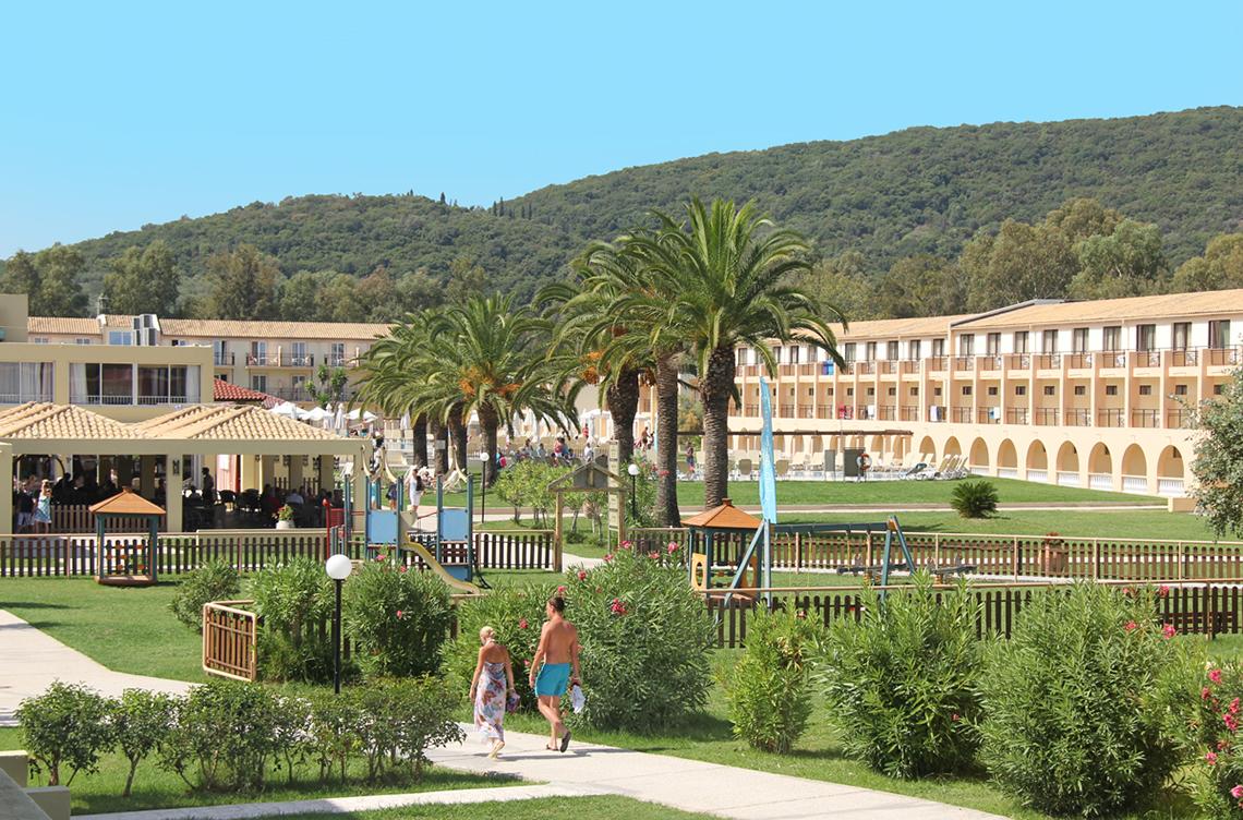 Außenbereich des Messonghi Beach Holiday Resorts mit Gästen, Palmen und einem Spielplatz.