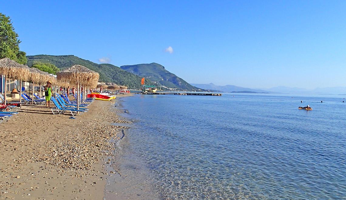 Strand des Messonghi Beach Holiday Resort mit Sonnenliegen, Sonnenschirmen und Booten im Wasser