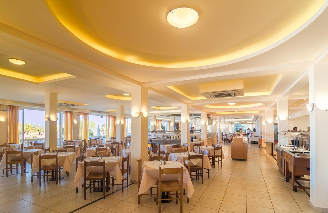 Innenansicht des Restaurants im Messonghi Beach Holiday Resort mit gedeckten Tischen und warmer Beleuchtung.