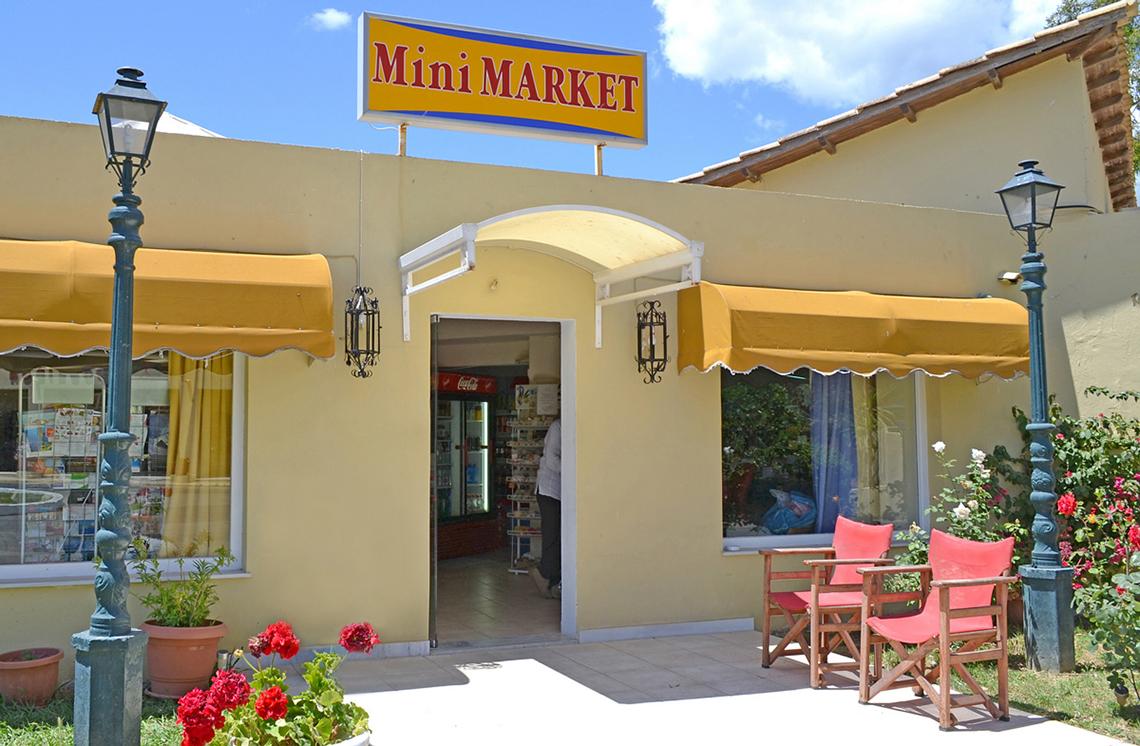 Außenansicht des Mini Markets vor dem Messonghi Beach Holiday Resort mit gelben Vordächern und roten Stühlen.