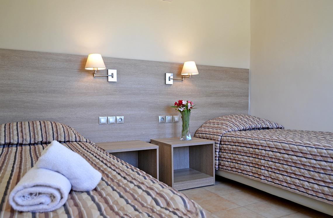Zwei Betten im Hotelzimmer von Messonghi Beach Holiday Resort mit gestreiften Laken und Kissen, Nachttischen und Nachtlampen an der Wand.