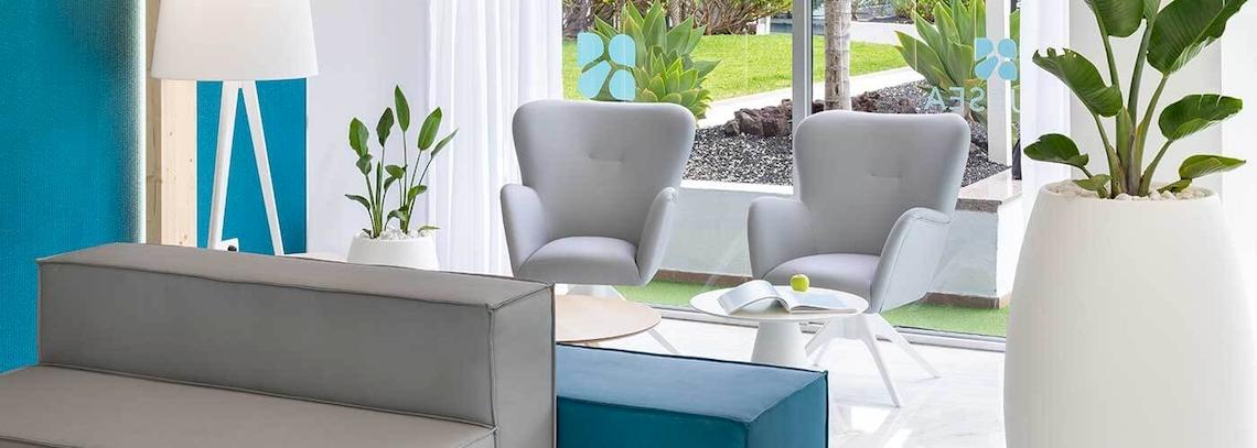 Empfangsbereich des Bluesea Interpalace Hotels mit grauen Sesseln, einem blauen Hocker, Tischen und Pflanzen.
