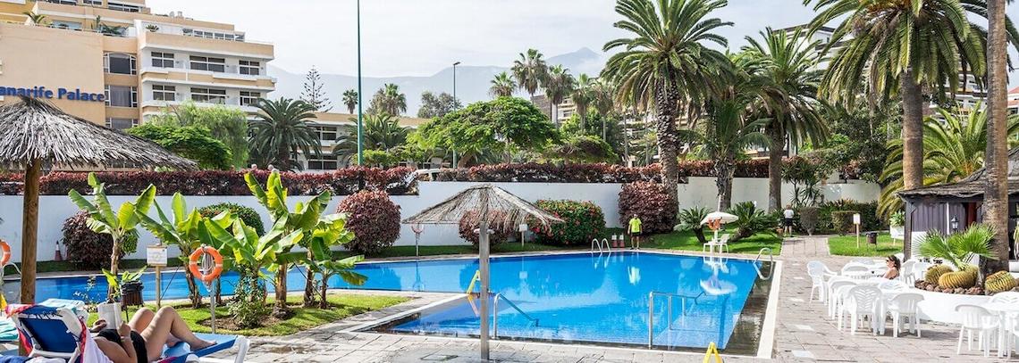 Außenpool des Hotels BLUESEA Interpalace mit Lounge-Stühlen und Sonnenschirmen, umgeben von Palmen und Pflanzen.