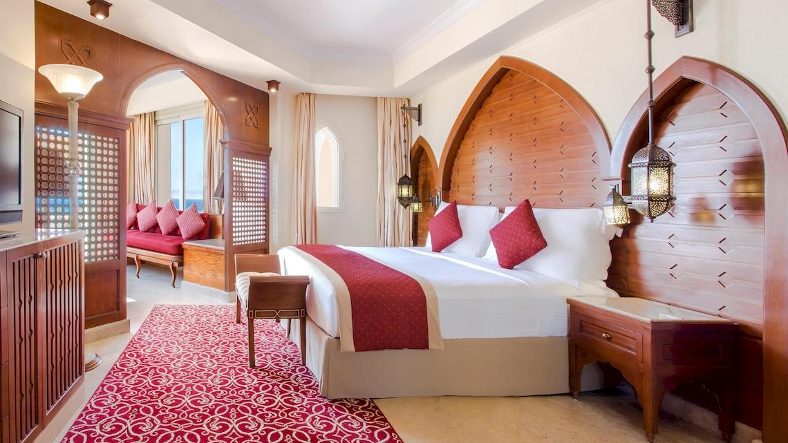 Schlafzimmer im Kempinski Hotel Soma Bay mit rotem Teppich und großen Bett.