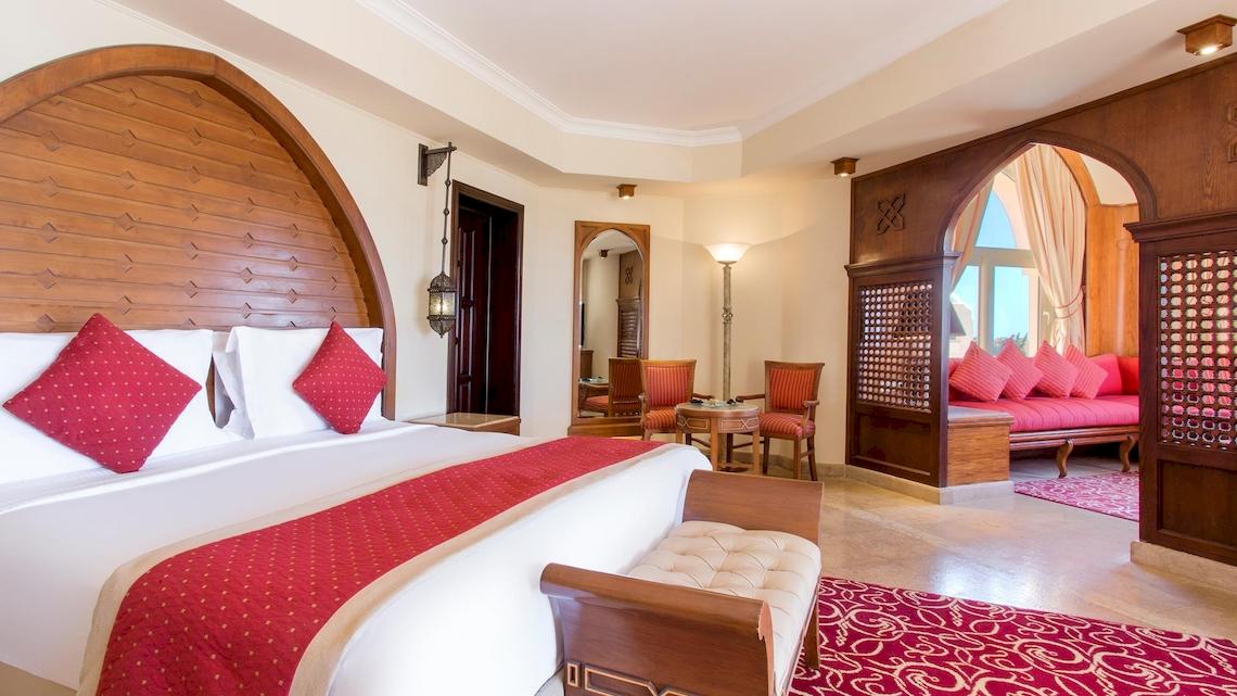 Luxuriöses Hotelzimmer im Kempinski Hotel Soma Bay mit rotem Bett, weißen Kissen und Holzmöbeln.