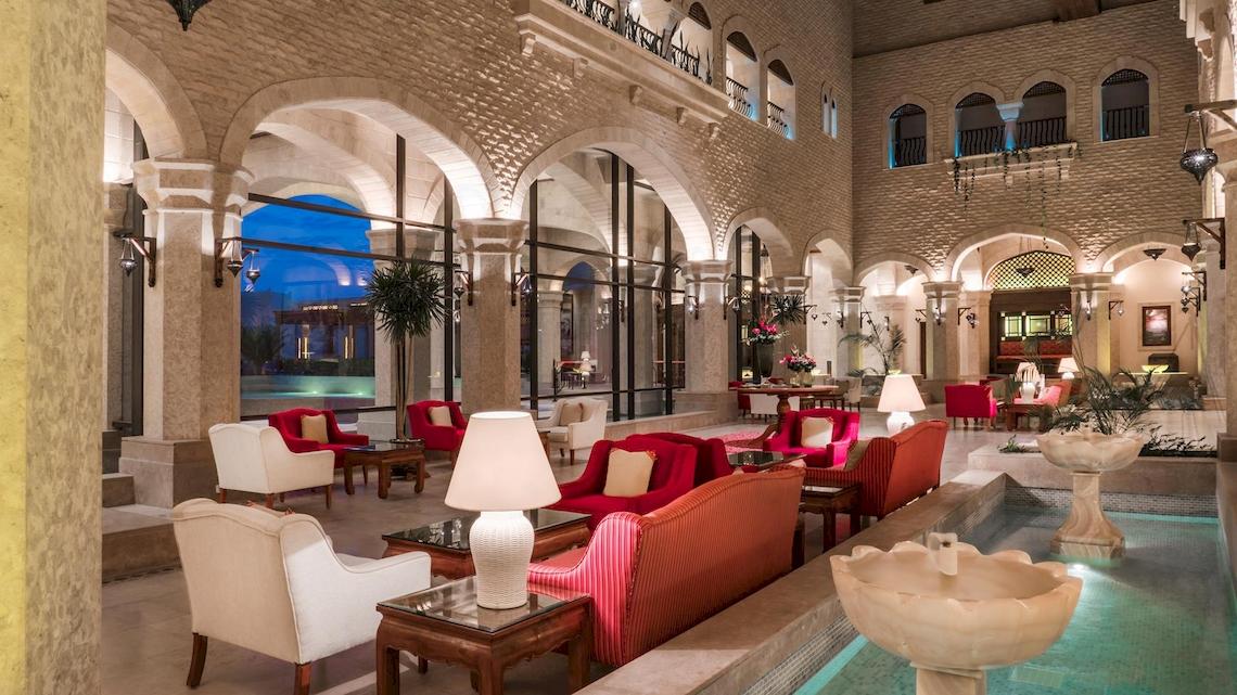 Lobby des Kempinski Hotels Soma Bay mit weißen und roten Möbeln, Lampen und einem Wasserbrunnen.