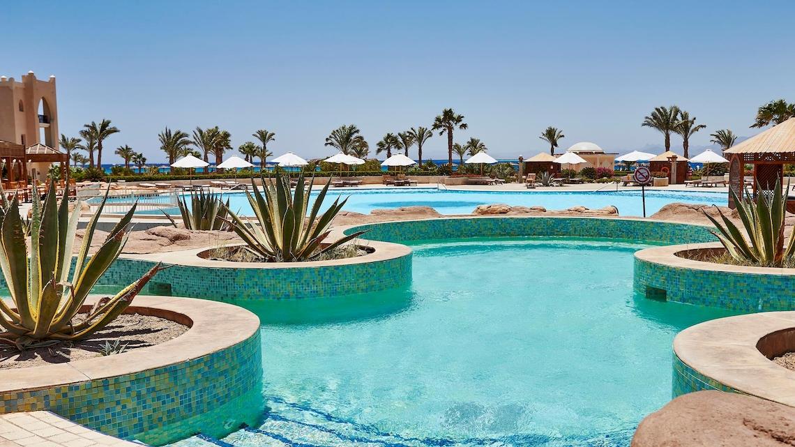 Außenpool des Kempinski Hotels Soma Bay mit mehreren Pflanzen und weißen Sonnenschirmen.