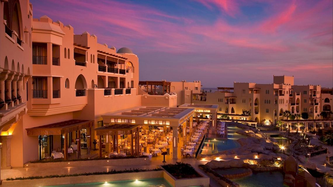 Luftaufnahme des Kempinski Hotels Soma Bay bei Sonnenuntergang mit rosa Himmel und beleuchtetem Poolbereich.