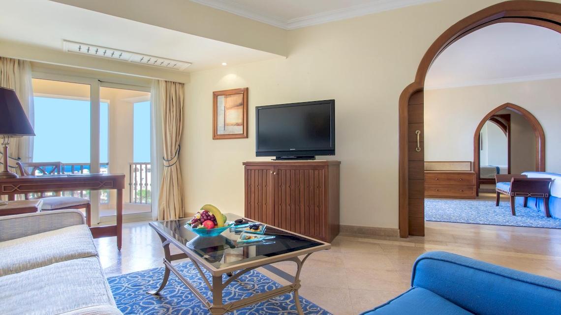 Hotelzimmer im Kempinski Hotel Soma Bay mit Fernseher, Tisch, Sessel und Aussicht.