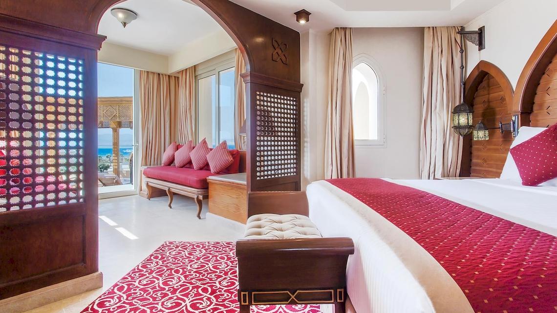 Innenansicht der Suite im Kempinski Hotel Soma Bay mit einem großen Bett, einem roten Teppich und einem Fenster mit Meerblick.