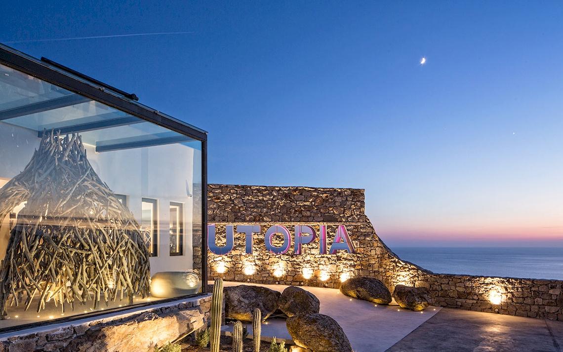 Außenbereich des Myconian Utopia Resorts mit Steinmauer, Steinen und Meeresblick bei Sonnenuntergang