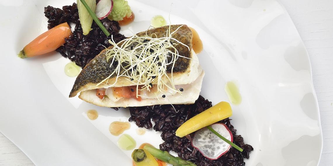 Gegrillter Fisch auf schwarzem Reis und Gemüse auf einem weißen Teller