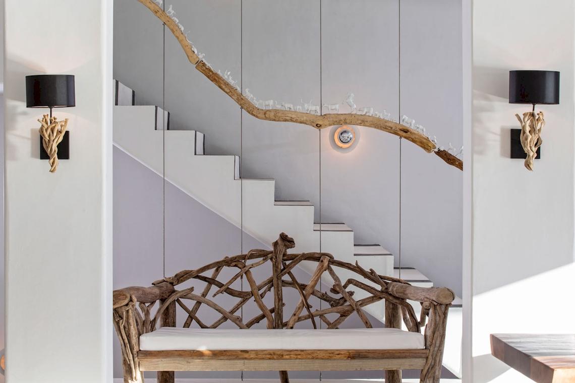 Eine Holzbank im Eingangsbereich des Myconian Utopia Resorts mit einer Treppe im Hintergrund und dekorativen Wandleuchten.