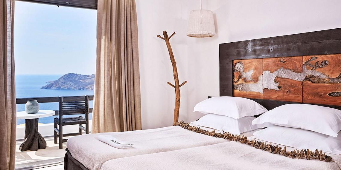 Doppelbettzimmer im Myconian Utopia Resort mit Meerblick, weiße Laken, Holzkopfteil und Aussicht auf das Meer und eine Insel.