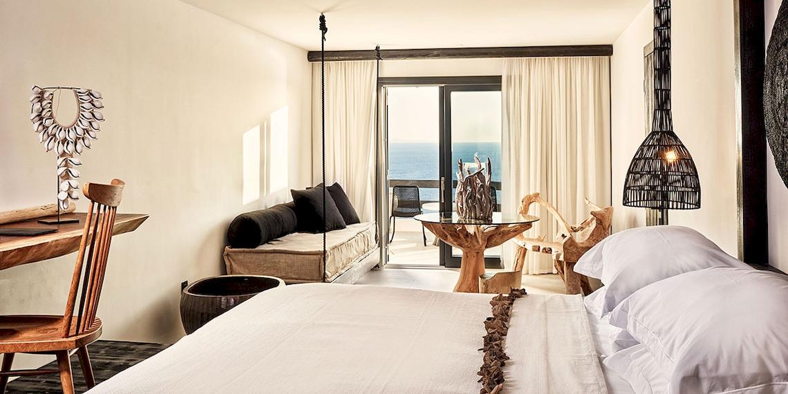 Innenansicht eines Schlafzimmers im Myconian Utopia Resort mit Meerblick, Holzmöbeln und einem Bett.