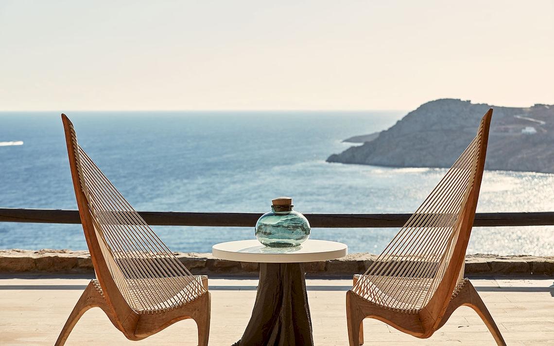 Aussicht auf das Meer vom Myconian Utopia Resort mit zwei Holzstühlen und einem kleinen Tisch.